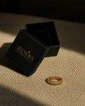 Gold ring on a textured surface next to an open black box with 'Zeenora' branding.